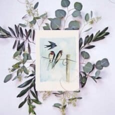 An enchanting Barn swallow Print capturing two birds sitting on a wire, surrounded by delicate eucalyptus leaves.