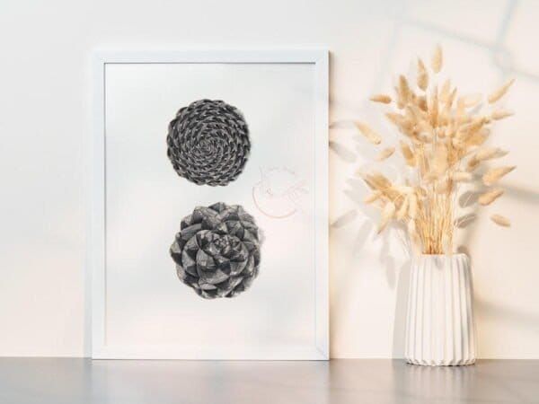 A black and white Pine cone print of two pine cones on a table next to a vase.