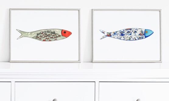 Two framed illustrations of fish, one filled with urban images and the other with colorful patterns, hung above a white cabinet.