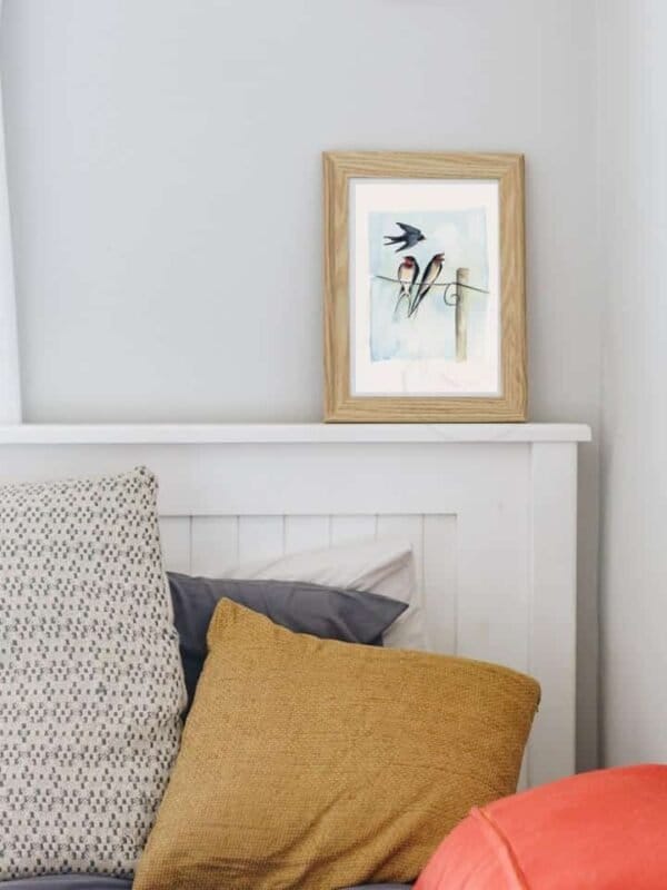 A bedroom with a bed, pillows, and a Barn Swallow Print from Portugal Shop.