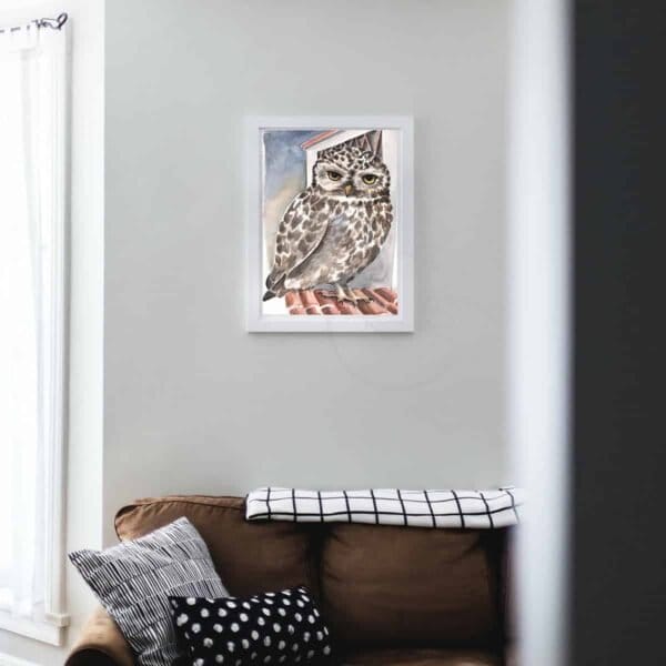 An owl sits on top of a couch in a living room, portrayed in a stunning Little owl print.