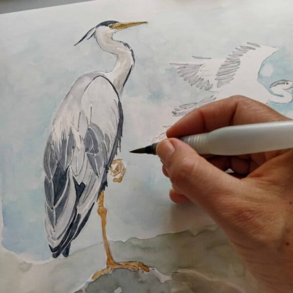 A person is creating a detailed fine art print of a grey heron using a pen.